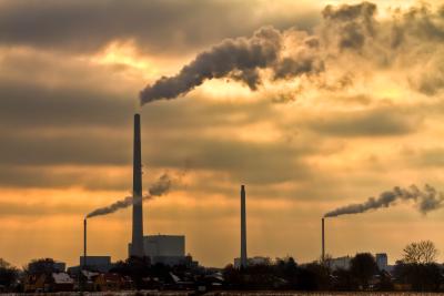 Fotoet viser et panorama af fire  industriskorstene, hvorfra der kommer hvid røg op mod en overskyet himmel.